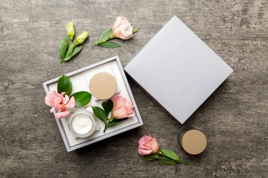 Composition with cosmetic products and beautiful roses on cement background. Flat lay.