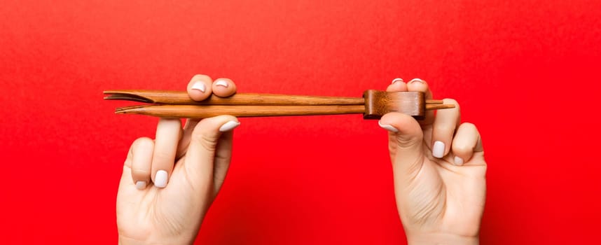 Crop image of two female hands holding chopsticks on red background. Ready to eat concept with copy space.