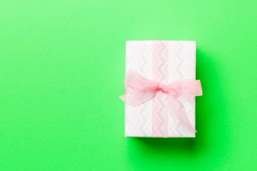 wrapped Christmas or other holiday handmade present in paper with pink ribbon on green background. Present box, decoration of gift on colored table, top view with copy space.