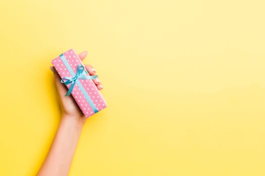 Woman arms holding gift box with colored ribbon on yellow table background, top view and copy space for you design.