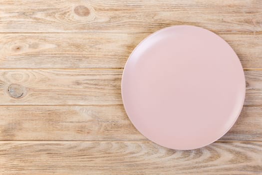 Directy above Empty pink matte dish for dinner on wooden orange background with copy space.