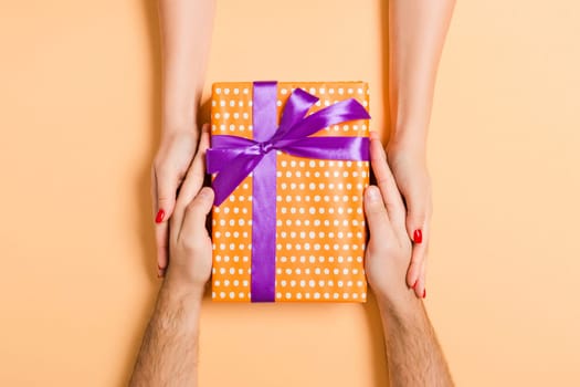 Top view of giving and receiving a gift on colorful background. Present in male and female hands. Love concept. Close up.