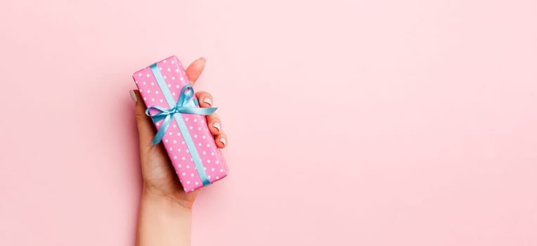 Female's hands holding striped gift box with colored ribbon on living coral background. Christmas concept or other holiday handmade present box, concept top view with copy space.