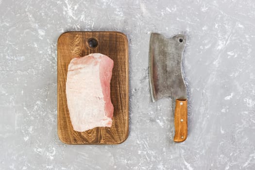 Raw cut of pork shoulder on board with knife or Kitchen ax. cleaver with fresh raw meat on gray concrete background.