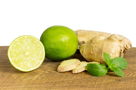 detail of whole and cut fresh ginger with lime on wooden cutting board isolated