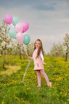 girl with colorful balloons in a blooming garden with trees