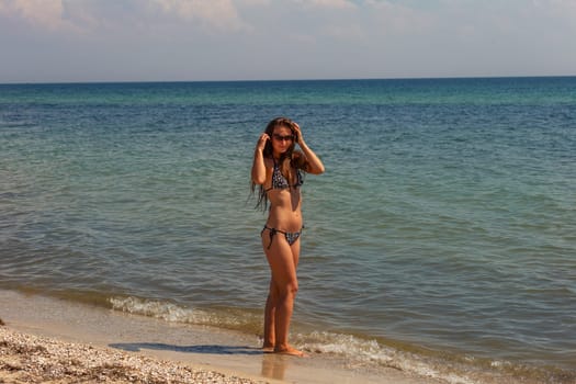 a girl in a swimsuit and sunglasses stands on the background of the sea