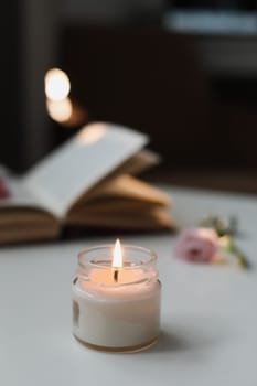 Still life details in home interior of living room. Eco-friendly fragrance for the home. Cozy home concept. Open book with flower, burning candle with smoke