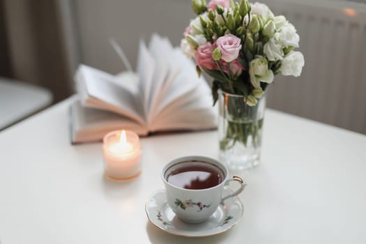 Home cozy still life. Romantic background with cup of tea, rose flowers and open book over white table