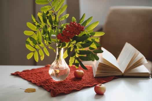 autumn still life with a rowan branch in a vase and a book and apples in a cozy home interior