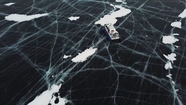 Snow air motion boat goes on big snow field of a frozen lake. Aerial view of icy surface of the Baikal lake near cliffs of Olkhon Island.