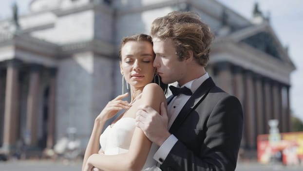 Beautiful couple of newlyweds embracing on background of city. Action. Photo shoot for newlyweds in urban environment. Beautiful newlyweds embrace in city with old architecture.