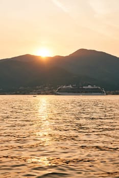 White cruise ship sails on the sea against the backdrop of mountains at sunset. High quality photo