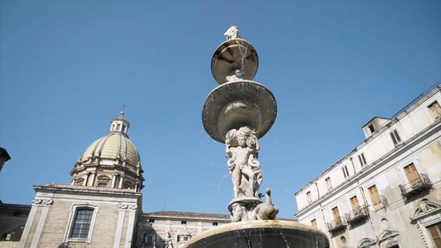 Bottom view of a beautiful fountain in front of Cathedral. Monumental fountain with a sculpture of a boy near the temple with a dome on blue clear sky background.