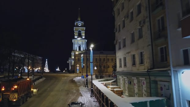 Winter evening landscape of the city. Clip. A street with tall residential buildings next to a road with cars on which lanterns shine and a white temple is visible. High quality 4k footage