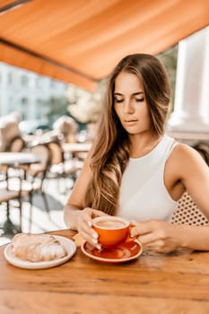 Portrait of happy woman sitting in a cafe outdoor drinking coffee. Woman while relaxing in cafe at table on street, dressed in a white T-shirt and jeans.