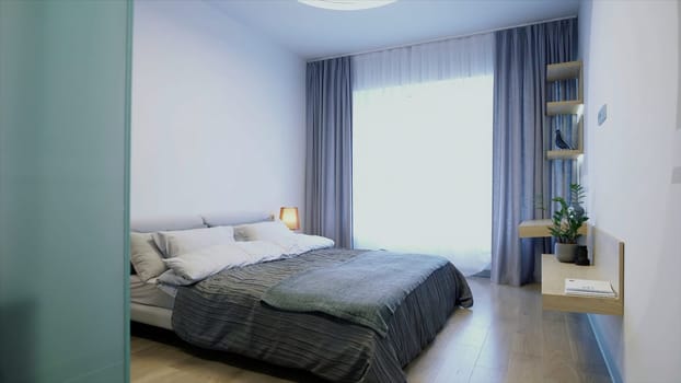 New hotel room with a bedroom full of sunlight. Video. Beautiful interior with a double bed, lamp, large window and shelves on the wall