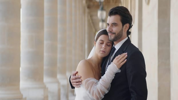 Woman embraces man in wedding dresses. Action. Woman snuggled up to husband on street. Happy newlyweds in outfits hug on summer day.