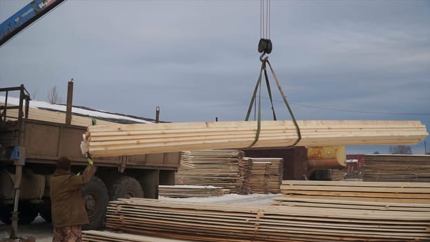 Wooden planks are lifted by crane for transportation. Clip. Loading of wooden boards for transportation. Loading crane with workers lift boards at wood company.