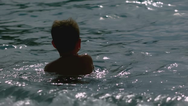 Boy swims in sea with waves. Creative. Boy swims alone on sea in sunny weather. Boy is resting on sea and swimming with waves and splashes.