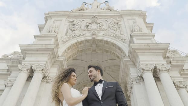 Beautiful couple on background of arch. Action. View from below of elegant couple at Arc de Triomphe. Beautiful couple in love in costumes at ancient building.