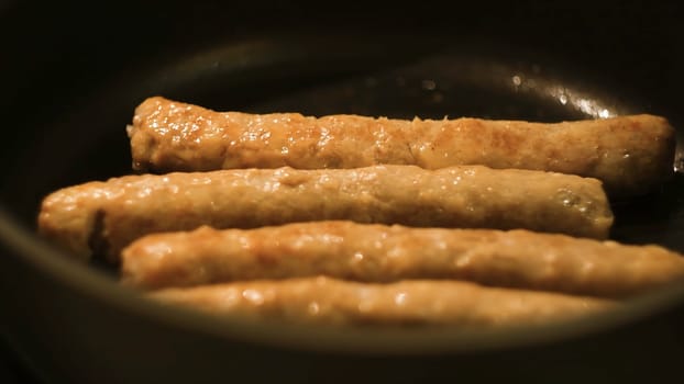 Close-up of meat sausages being fried in a frying pan. Concept. Close up view of sausages being fried in a pan. Pan with oil over a gas stove.