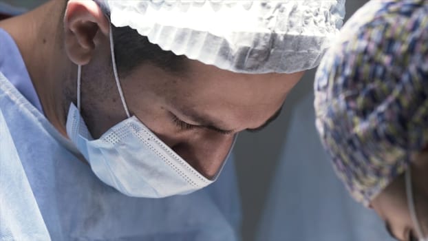 Close up of heads of male surgeons wearing protective masks surgical caps in a hospital operating theater. Concept of medicine and health.