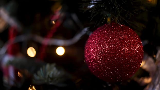 Decorated Christmas tree on blurred, sparkling and fairy background, merry christmas and happy new year concept. Close up for red shining ball and illuminated garland with flashlights.