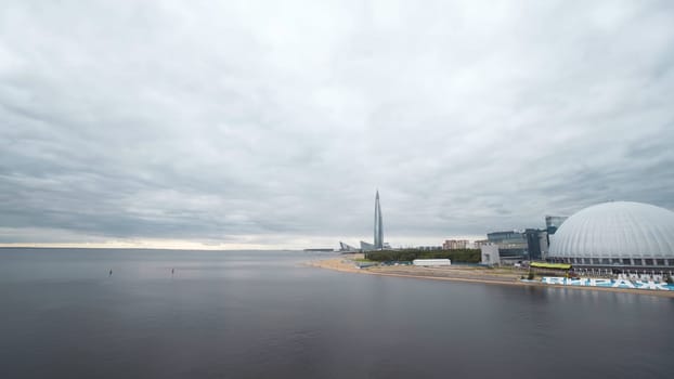 Top view of modern city on sea coast on background of cloudy sky. Action. Sea panorama with city on coast in cloudy weather. Tourist town on coast of sea reflecting gray sky.