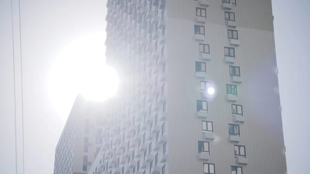 Multi-storey building on background of sun and clear sky. Action. Bottom view of beautiful residential building on background bright sun and sky.