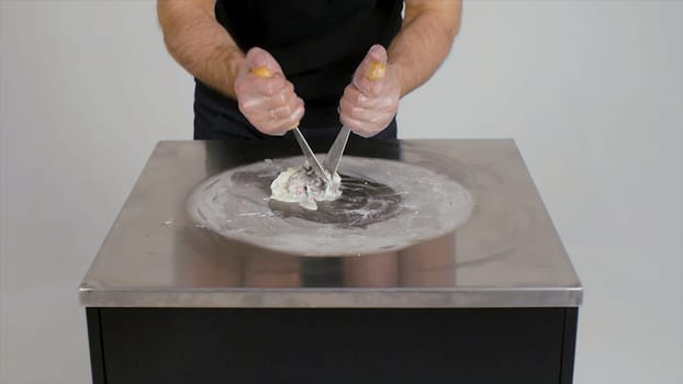 Cooking natural fruit ice cream in Thai style. Clip. Making ice cream rolls with passion fruit on cold plate. Making ice cream rolls on cold plate. Close up. Thai style stir-fried rolled ice cream being prepared. Exotic hand-made frozen dessert being made on steel plate iced grill
