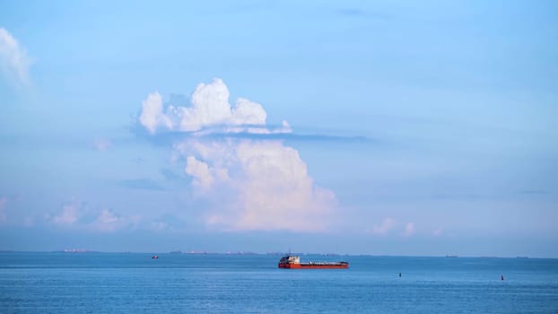 Breathtaking seascpe with a sailing red barge on blue cloudy sky on the background, water transport concept. Cargo ship barge on the sea horizon in a summer sunny day.