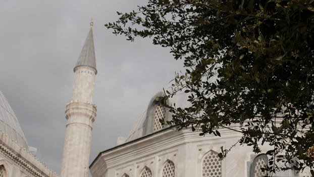 Minaret of a mosque on a cloudy sky background. Action. Summer green trees and mosque building