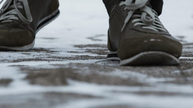 Close-up of male legs in winter shoes walking on snow. View of walking on snow with Snow shoes and Shoe spikes in winter. Men's legs in boots close up the snow-covered path in the winter forest.