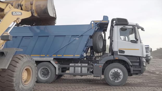 Russia, Moscow - May 7, 2022: Excavator loads dump truck with earth at construction site. Scene. Trucks are working and clearing construction site. Excavator pours earth into dump truck.