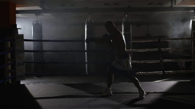 Fighter shadowboxing on training ring. Professional fighter. Male boxer in training sportswear, an exercise in sports hall, fight with a shadow in ring, Strike testing 4K