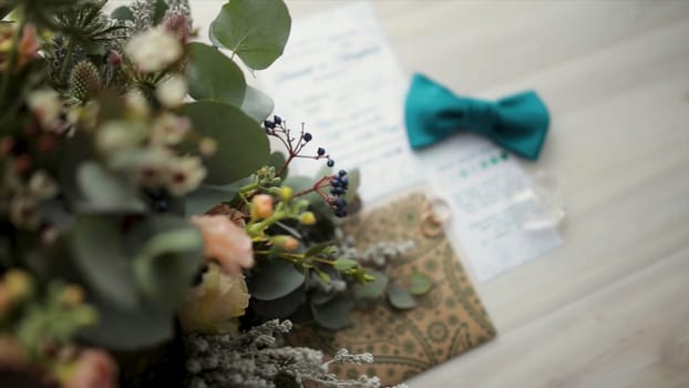 Accessories for the wedding ceremony. Closeup of elegant stylish brown male accessories on wooden background. Top view of bow-tie, belt, floral corsage, golden rings. Wedding bow tai with flower. Preparation for wedding concept