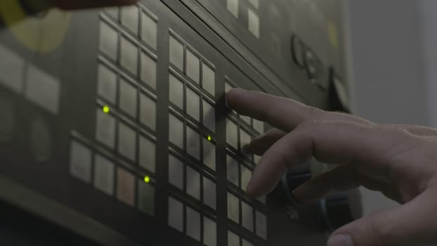 Close up of a hand presses buttons on the control panel of industrial equipment. Side view of male hand pushing the button at the factory panel.