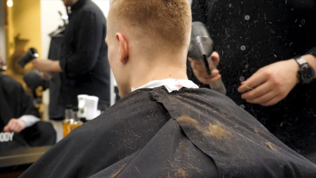 Barber cutting hair with scissors and hair flying in the air in slow motion. Back view of man in barber shop and flying hair in slow motion. Close-up back view of young bearded man getting beard haircut by hairdresser at barbershop