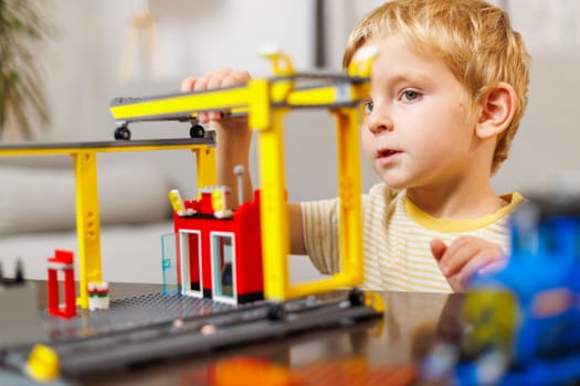 Child boy playing and building with colorful plastic bricks at the table. Early learning and development