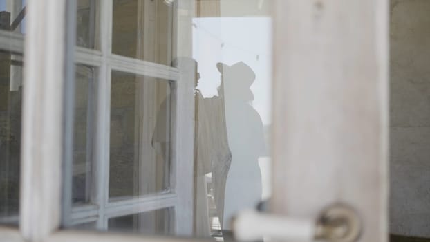 View through the window with translucent curtains to the people in a room. Action. Women silhouettes inside the building