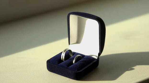 Ring in the box on wooden table. Stock. Wedding rings in a case on the table illuminated by sunlight.
