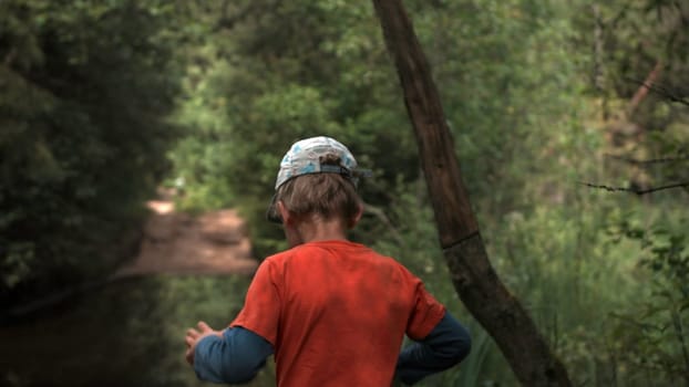 A little boy . Creative. A child in bright summer clothes walking through the forest next to a beautiful small lake. High quality FullHD footage