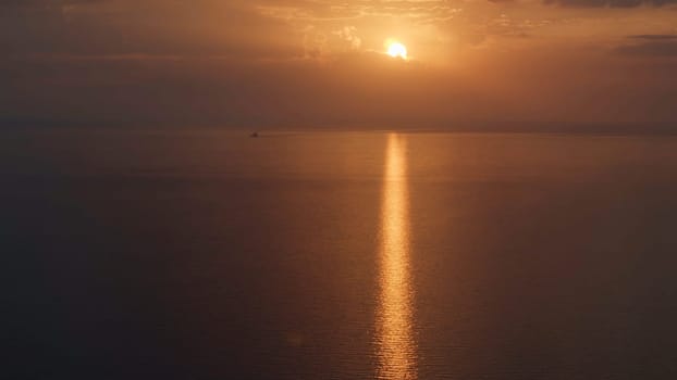 Aerial view of a golden sunset sky background with evening clouds over the sea. Stunning sky clouds in the sunset with a bright sun path on the sea surface.