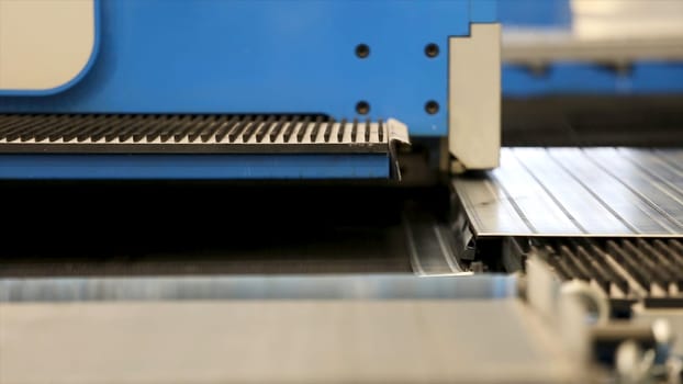 Cutting holes perforation stamping of metal sheets on industrial CNC machine. Close-up shot of a CNC coordinate punching press perforates metal sheet. Automation of work. Refrigeration and ventilation equipment.