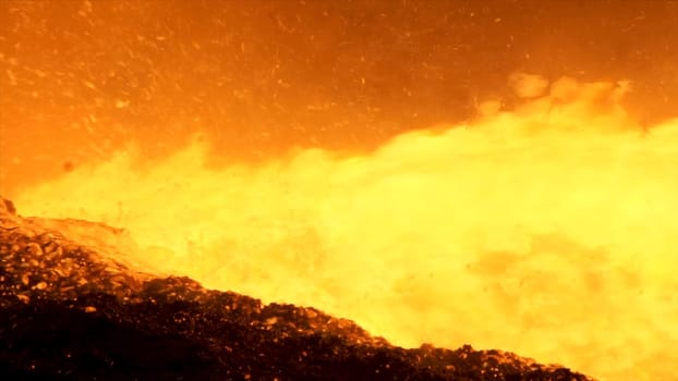 Close up for liquid metal flowing from blast furnace at the metallurgical plant, heavy industry concept. Pouring molten steel from a pipe with many sparkles flying into the sides
