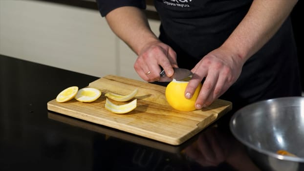 Close up of a male chef peeling a fresh orange fruit with a steel knife on a wooden board. Art. Concept of vegan food, vitamins, and cooking