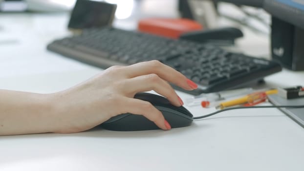 Close-up of woman working at computer in office. Creative. Woman drives computer mouse at desk. Woman's hand with manicure howls with computer mouse.