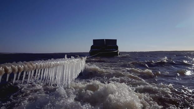Large barge at the North Pole. CLIP. In the foreground Rope with icicles. In the background, a heavy barge in ice water is in focus. A ship pulling a barge in tow.