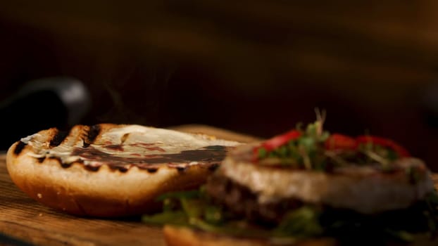 Male chef hands preparing burger in dark room and adding liquid red wine sauce on a toasted burger bun with a teaspoon. Foodporn and gastronomy concept.